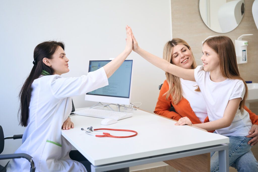 Qualified Woman Pediatrist Exchanging High Five With Little Girl Patient